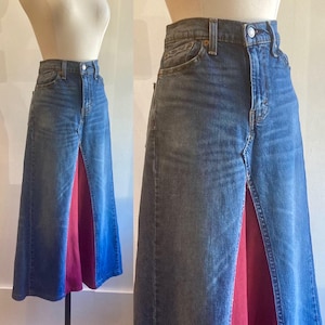 May include: A denim skirt with a front slit and a red and pink panel sewn into the bottom. The skirt is a maxi length and has a high waist.