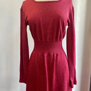 May include: A long-sleeved, burgundy knit dress with a fitted bodice and a flowing skirt. The dress has a subtle shimmer and a slightly textured fabric.