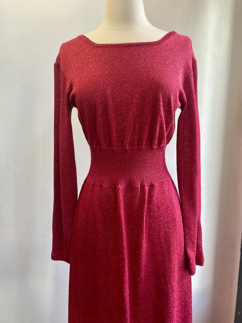 May include: A long-sleeved, burgundy knit dress with a fitted bodice and a flowing skirt. The dress has a subtle shimmer and a slightly textured fabric.