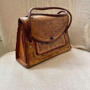 Pode incluir: Bolsa de m&atilde;o vintage em couro castanho com design floral em relevo. A bolsa apresenta uma al&ccedil;a superior, fecho de aba e costuras decorativas. A bolsa retangular parece estar em bom estado.