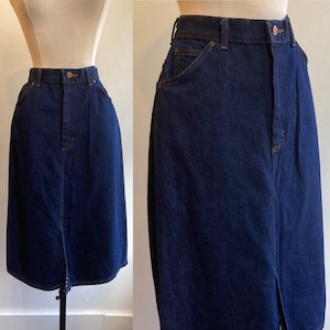 May include: A dark wash denim skirt with a front slit. The skirt has a button and zipper closure, belt loops, and front and back pockets. The skirt is displayed on a mannequin. The skirt's length is approximately 30 inches.