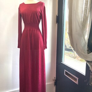 May include: A long, burgundy knit dress with a fitted bodice and a flowing skirt. The dress has a square neckline and long sleeves.