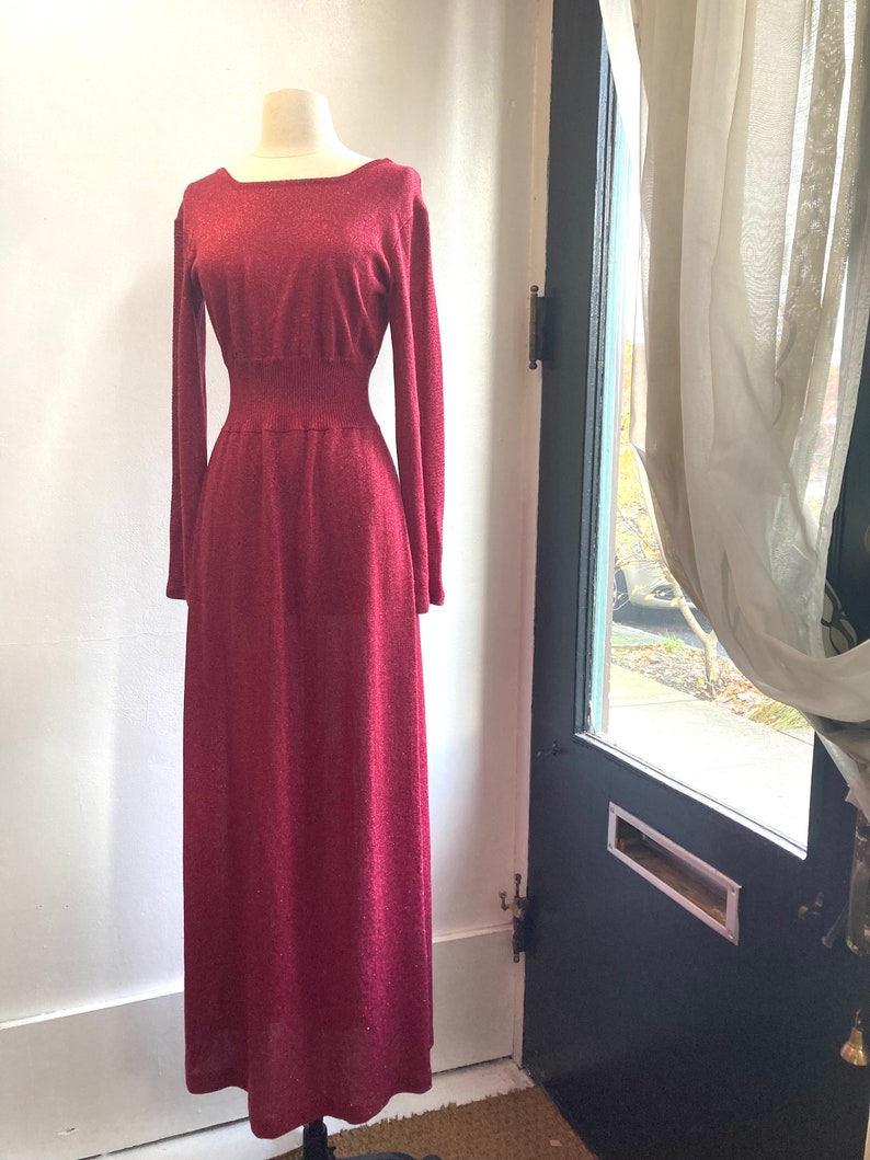 May include: A long, burgundy knit dress with a fitted bodice and a flowing skirt. The dress has a square neckline and long sleeves.