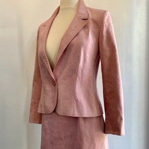May include: A dusty rose-colored suede skirt suit with a single button closure on the jacket.
