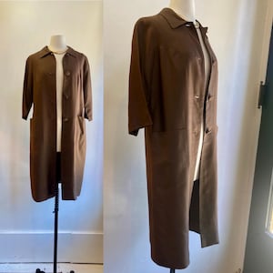 May include: A brown knee-length coat with three-quarter sleeves and a collared neckline. The coat has a button-up front and two front pockets. The coat is displayed on a mannequin. The coat is a vintage style.