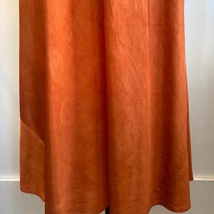 May include: A rust-colored maxi skirt with a flowing, A-line silhouette. The skirt is made of a soft, lightweight fabric and has a simple, elegant design.