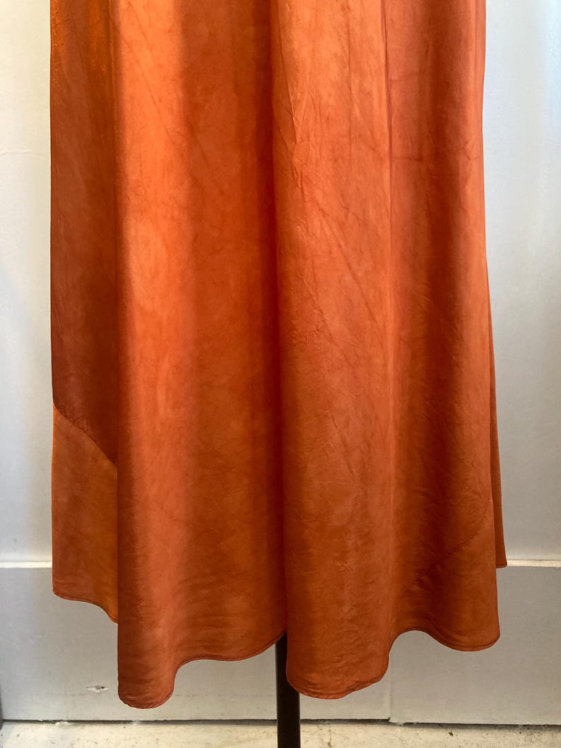 May include: A rust-colored maxi skirt with a flowing, A-line silhouette. The skirt is made of a soft, lightweight fabric and has a simple, elegant design.