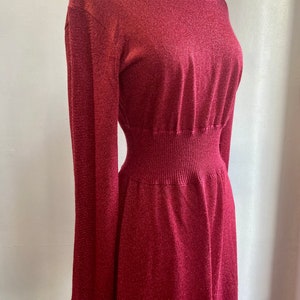 May include: A long-sleeved, burgundy knit dress with a fitted bodice and a flowing skirt. The dress has a subtle shimmer and a stretchy waistband.