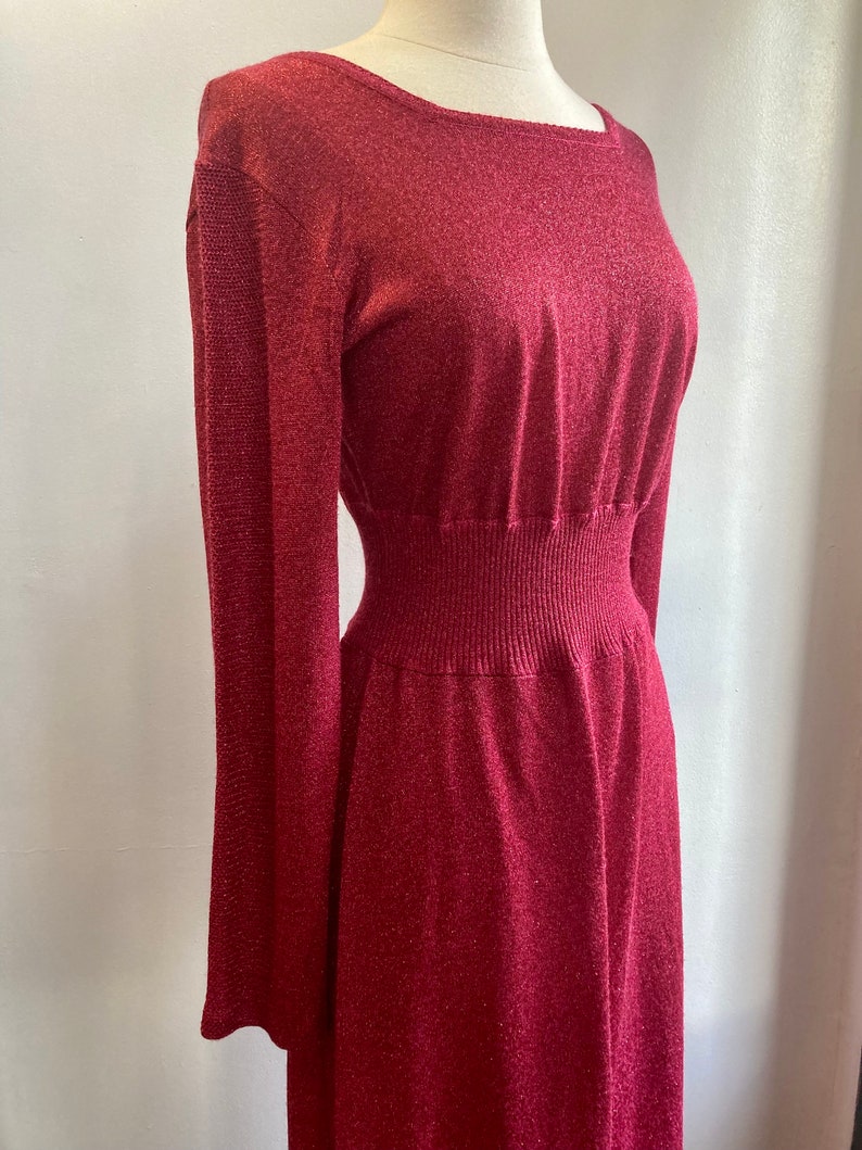 May include: A long-sleeved, burgundy knit dress with a fitted bodice and a flowing skirt. The dress has a subtle shimmer and a stretchy waistband.