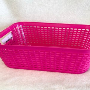 May include: A bright pink plastic storage basket with a woven design. The basket has two handles on the sides.