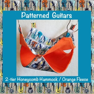 May include: A two-tiered pet hammock with a honeycomb pattern and orange fleece lining. The hammock is suspended from two metal hooks. The fabric features a pattern of colorful guitars.