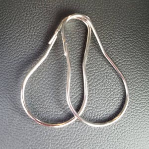 May include: Two silver shower curtain rings, shaped like a teardrop, are lying on a textured gray surface.