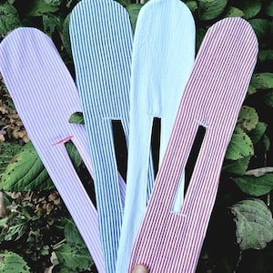 Puede incluir: Cuatro accesorios de peinado de tela en forma larga, plana y redondeada con una ranura central. El conjunto incluye una pieza a rayas lavanda, una a rayas azules, una blanca lisa y una a rayas rojas, todas con una abertura cosida.
