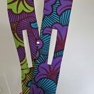 May include: Two fabric hair accessories with a floral pattern in purple, blue, green, and maroon. Each piece has a white rectangular opening and a small tag with a flag. The accessories are held up against a white background.