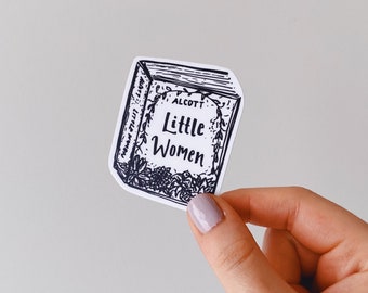 May include: A black and white sticker of a book cover with the title "Little Women" by Louisa May Alcott. The book cover is surrounded by a floral design.