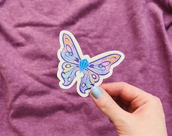 May include: A colorful butterfly sticker with a blue gem in the center. The butterfly has intricate details and a white background.
