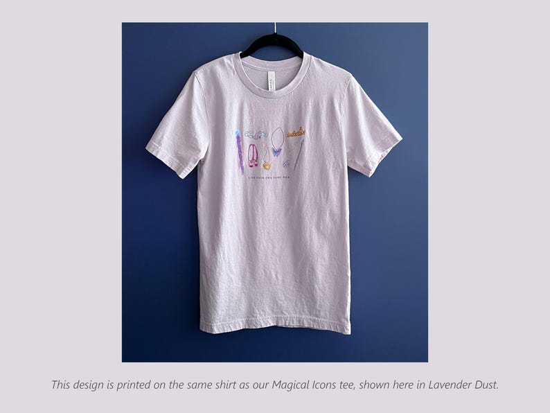 Puede incluir: Camiseta lila claro con cuello redondo, con una colorida ilustraci&oacute;n de accesorios. El dise&ntilde;o incluye una varita, zapatos, un collar y una corona. El texto "Live your own fairy tale" est&aacute; impreso debajo.