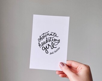 May include: A white card with black calligraphy that reads "obstinate headstrong girl" and "Jane Austen" in smaller font.