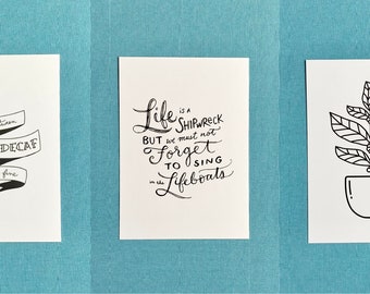 May include: Three white cards with black ink illustrations and text. One card reads "DEATH and DECAF, decaf is fine." Another says "Life is a shipwreck but we must not forget to sing in the lifeboats." The last card shows a coffee plant in a mug.