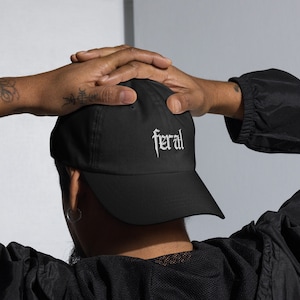 May include: A black baseball cap with a white embroidered "feral" logo. The cap is worn backwards on a person's head.