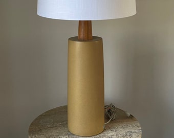 May include: A gold ceramic table lamp with a white linen lampshade and a wooden base.