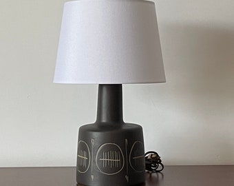 May include: A black ceramic table lamp with a white lampshade. The lamp base features a geometric design with circles and lines.