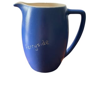 May include: A blue ceramic pitcher with a white rim and handle. The word "Ferryside" is written in white on the side of the pitcher.