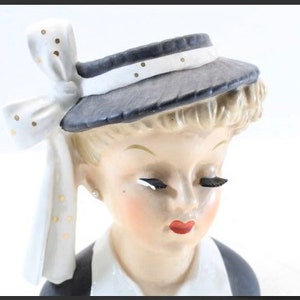 May include: A vintage ceramic figurine of a woman wearing a black and white hat with a white bow. The figurine has a white face with painted features and red lips.