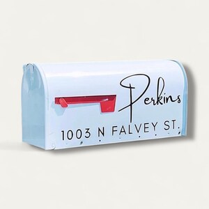 May include: White mailbox with a red flag and the name "Perkins" in black script. The address "1003 N FALVEY ST." is printed below the name in a black, sans-serif font. The mailbox is a classic, rectangular shape.