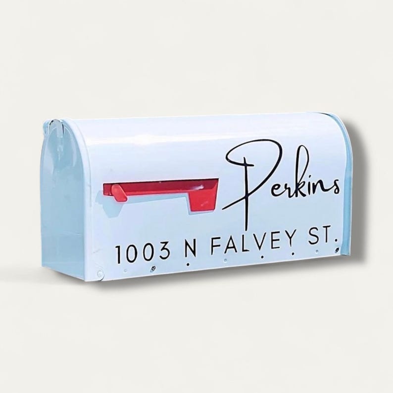 May include: White mailbox with a red flag and the name "Perkins" in black script. The address "1003 N FALVEY ST." is printed below the name in a black, sans-serif font. The mailbox is a classic, rectangular shape.