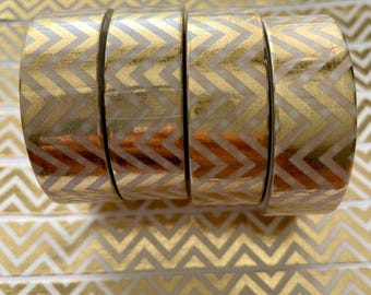 May include: Five rolls of decorative washi tape with a gold chevron pattern on a white background. The tape is arranged in a row, with the pattern visible on the rolls and the surface below. This tape is ideal for scrapbooking, crafting, and adding a touch of elegance to any project.