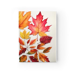 May include: A hardback journal featuring a vibrant illustration of various autumn leaves in shades of red, orange, yellow, and brown scattered across a white background. The cover displays detailed maple and serrated foliage patterns.