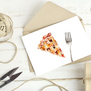 May include: A white card with a watercolor illustration of a slice of pie and a fork. The card is sitting on a wooden surface with a brown envelope, twine, and two brown paper hearts.