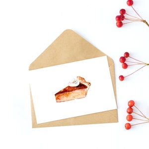 May include: A watercolor illustration of a slice of pumpkin pie with whipped cream on top. The pie is on a white card with a brown envelope behind it. There are red berries and branches in the background.