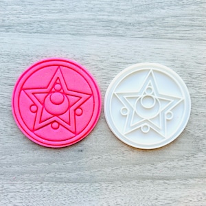 May include: Two cookie cutters, one pink and one white, shaped like the magical star from the anime Sailor Moon.