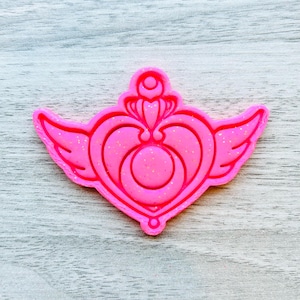 May include: Pink plastic cookie cutter shaped like a heart with wings and a crescent moon inside.