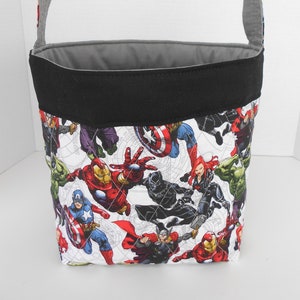 May include: A black and gray fabric tote bag with a white background and a print of various Marvel superheroes, including Iron Man, Captain America, Thor, Hulk, and Black Widow.