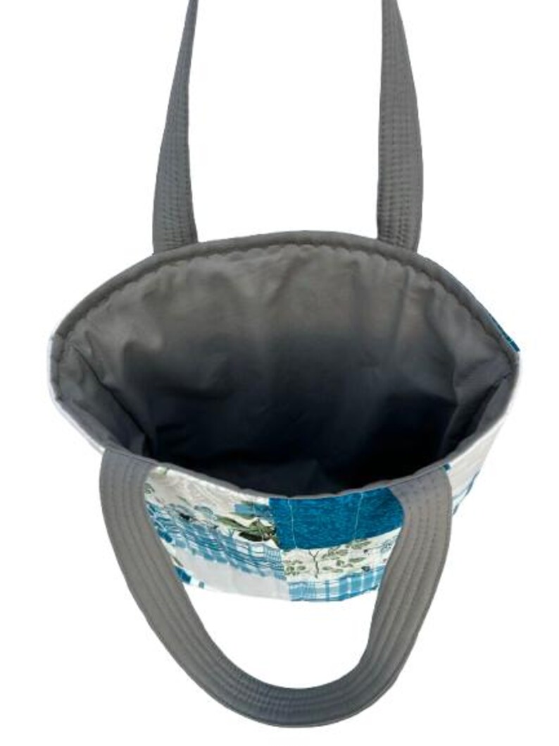 May include: A patchwork tote bag with gray handles and a gray interior. The exterior features a mix of blue, white, and green fabric squares. The bag is designed for carrying items.