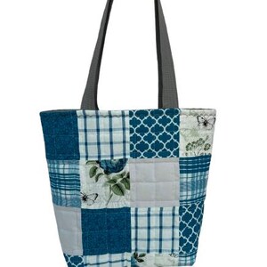 May include: A patchwork tote bag with gray handles. The bag features a variety of blue and white patterned squares, including floral, plaid, and geometric designs. Butterflies and flowers are also visible on some of the squares.