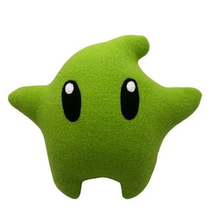 May include: A lime green star-shaped plush pillow with two large, oval black eyes and white highlights. The pillow has a textured surface and a small, pointed protrusion on top. The overall shape is reminiscent of a cartoon character.