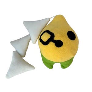 May include: A yellow and green plush toy shaped like a teardrop with black eyes and a black swirl design. The toy has a white tail with three triangular pieces.