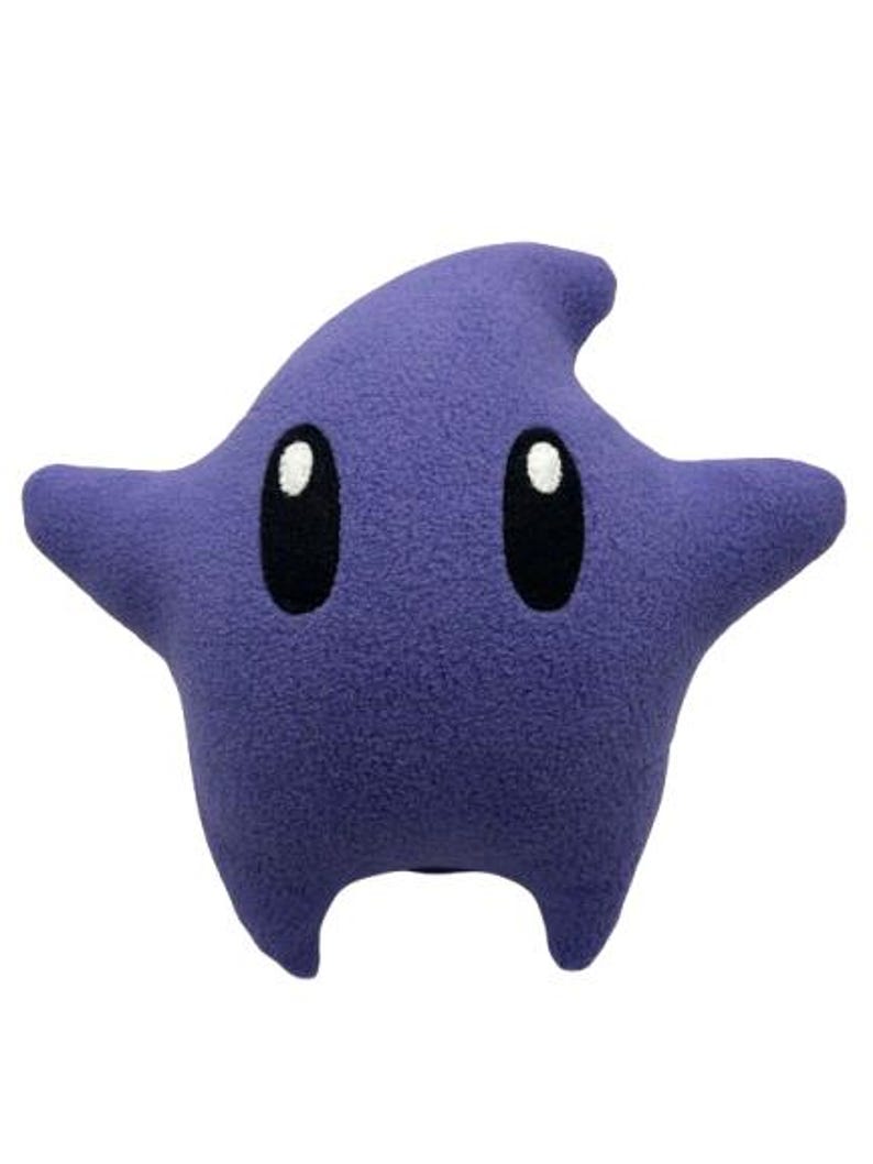 May include: A star-shaped plush pillow in a deep purple colour. It has two large, oval black eyes with white highlights. The design includes four points and a small, rounded bottom, resembling a cartoon character.