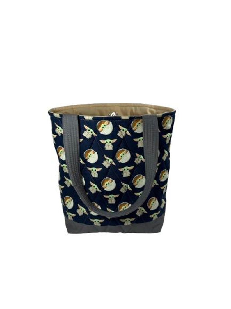 May include: A navy blue quilted tote bag featuring a repeating pattern of a character from a popular science fiction series. The bag has gray handles and a gray bottom. The interior is a light tan color.