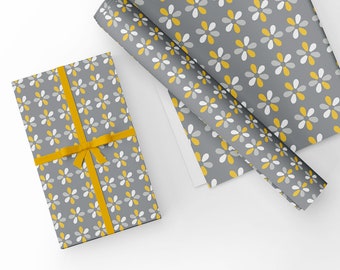 Pode incluir: Um papel de embrulho cinza e branco com um padrão de margaridas amarelas. Uma fita amarela está amarrada em torno de uma caixa de presente cinza embrulhada no mesmo papel.