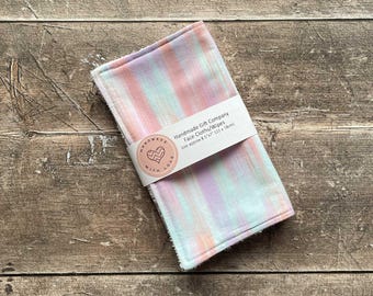 May include: A set of two pastel-colored face cloths with a striped pattern. The cloths are handmade and measure approximately 8.5 inches by 7 inches. The label reads "Handmade Gift Company Face Cloths/Wipes size approx 8.5"x7" (22 x 18cm)"