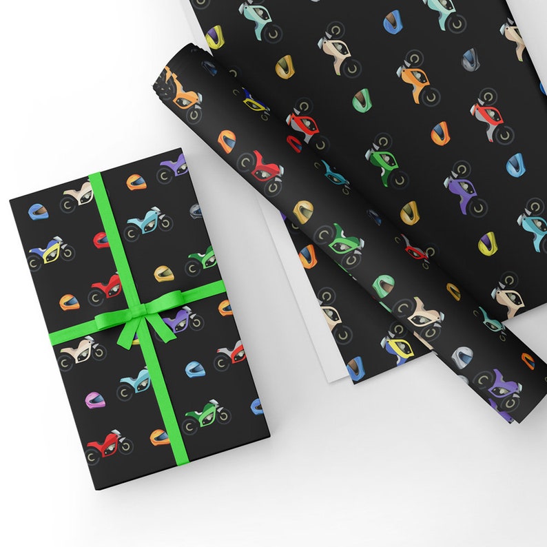 May include: Black gift wrap with a repeating pattern of colorful cartoon motorcycles and helmets. The gift wrap is rolled up and tied with a green ribbon.