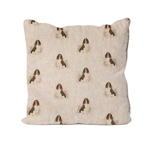 Può includere: Cuscino quadrato con un motivo ripetuto di cani Cavalier King Charles Spaniel. I cani sono raffigurati seduti con segni marroni, neri e bianchi. Il cuscino ha uno sfondo beige neutro.