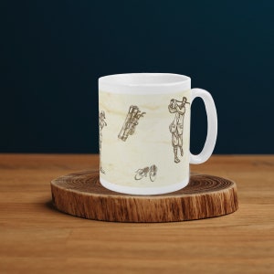 Puede incluir: Taza de cerámica blanca con una ilustración vintage de golfistas y palos de golf. El fondo es beige claro con un sutil efecto acuarela.
