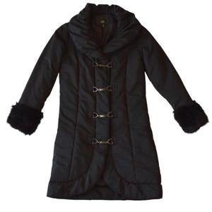 May include: A black winter coat with a large collar and three decorative clasps down the front. The coat has long sleeves with faux fur cuffs. The coat is a mid-length style.