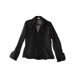 May include: Black long-sleeve blouse with a V-neck and ruffled detailing down the front. The blouse has a collared neckline and cuffs with subtle embellishments. The garment is hanging on a black hanger against a white background.